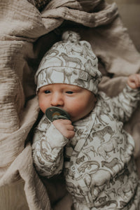 Een gezellig uitziende baby, gekleed in een Yumi Baby Overslagshirt Little Safari-onesie en bijpassend mutsje, rustend in een geweven mand op een zachte, milieuvriendelijke deken.