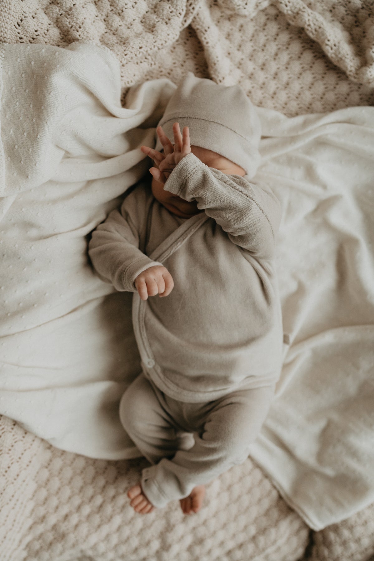 Baby in een zacht beige velvet fleece geboortepakje met muts.