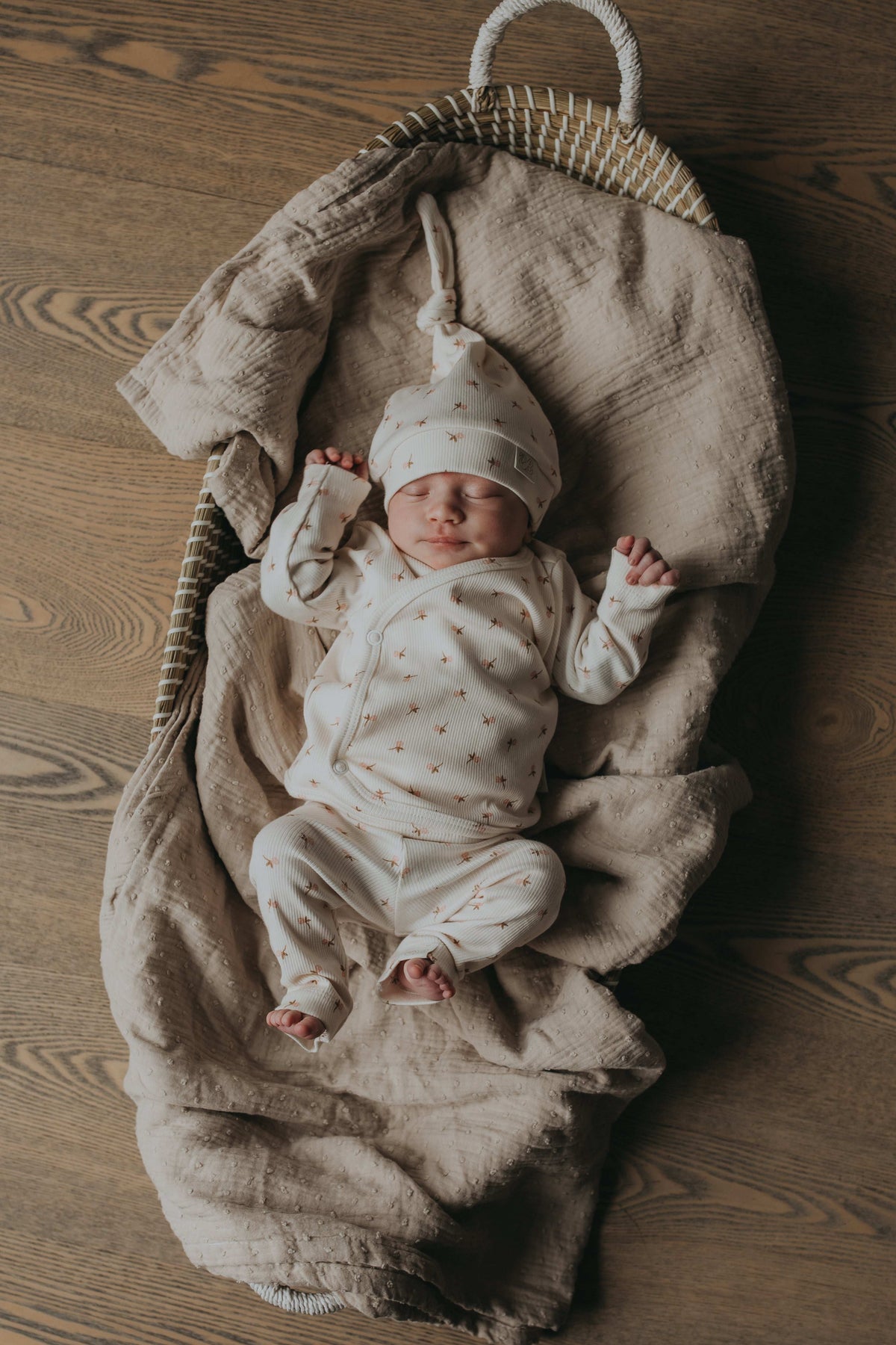 Een pasgeboren baby in een Broekje Tiny Tulip-outfit van Yumi Baby ligt op een crèmekleurige deken, geeuwend of huilend met kleine vuistjes bij het gezicht, en legt een kostbaar moment uit het vroege leven vast.