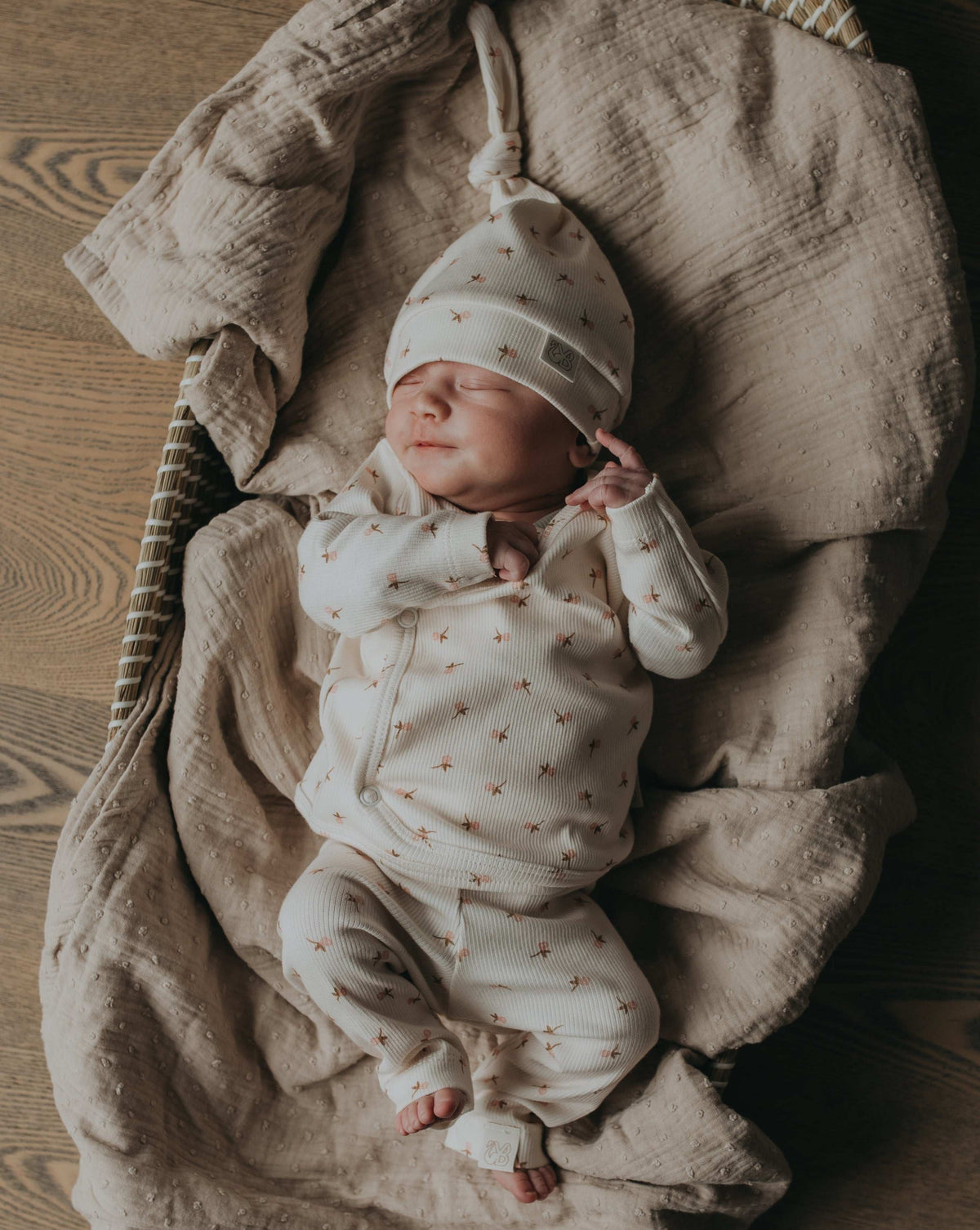 Een pasgeboren baby in een Broekje Tiny Tulip-outfit van Yumi Baby ligt op een crèmekleurige deken, geeuwend of huilend met kleine vuistjes bij het gezicht, en legt een kostbaar moment uit het vroege leven vast.