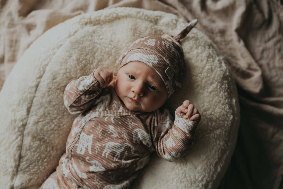 Een vredige pasgeboren baby slaapt knus in een geweven mand, gezellig gekleed in een Yumi Baby Boho Jungle overslagshirt en bijpassend mutsje, met zachte OEKO-TEX gecertificeerde katoenen dekens voor extra comfort.