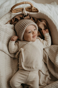 Baby met een gemeleerd newborn geboortepakje aan.