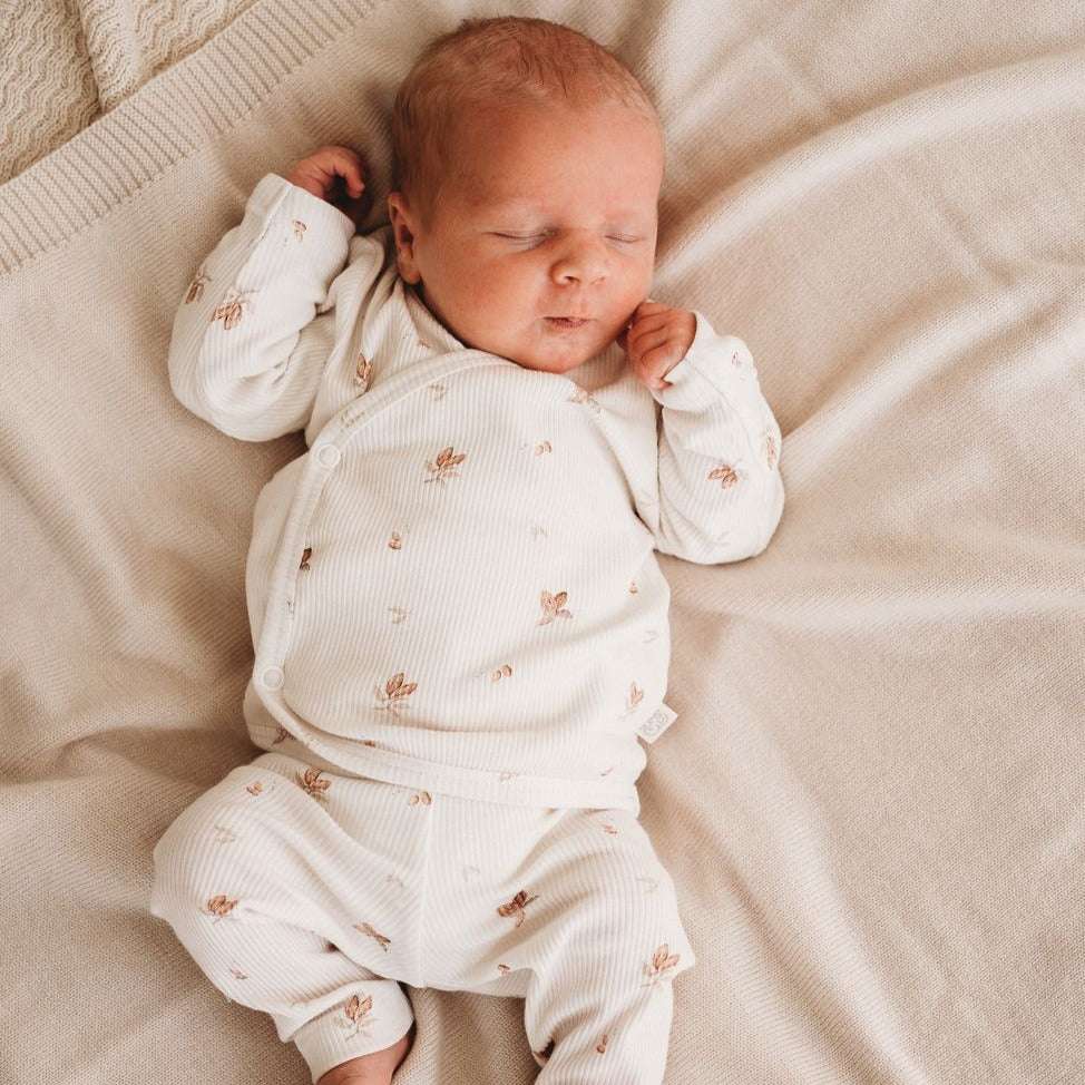 Vreedzame slaap: een pasgeboren baby rust rustig uit in een knusse outfit gemaakt van Yumi Baby's Overslagshirt Cocoa, die de pure onschuld van het vroege leven belichaamt.