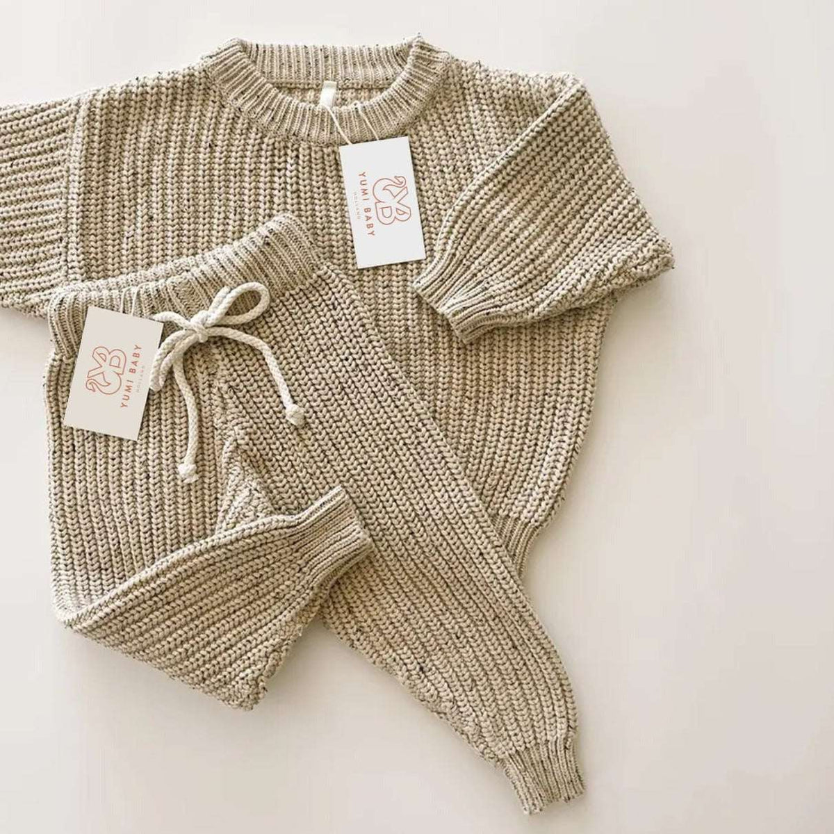 Een vredige baby slaapt heerlijk in een knus beige Yumi Baby Gebreide Set-outfit, met een zachte hoofdband en een klein knuffelkonijntje aan haar zijde.