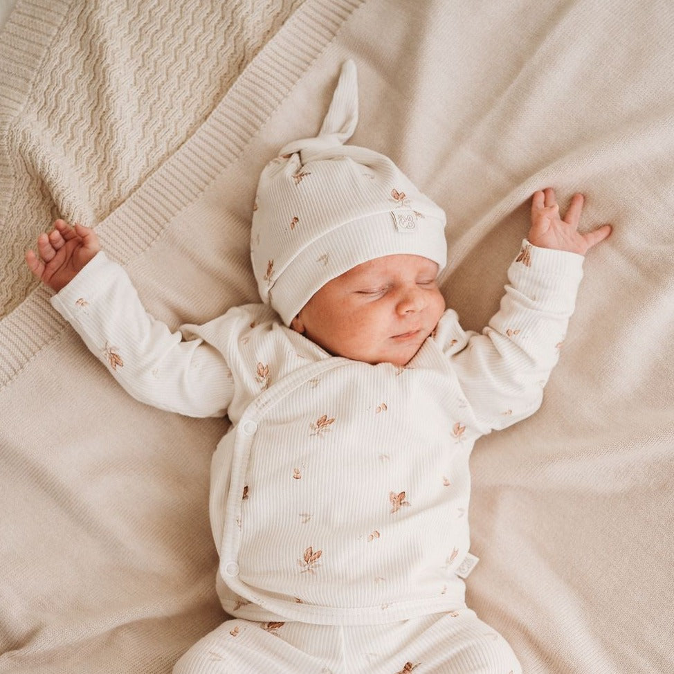 Een vredige pasgeboren baby in een Muts Cocoa-outfit en een hoogwaardige bijpassende Yumi Baby-muts, heerlijk slapend op een zachte, neutraal getinte deken.