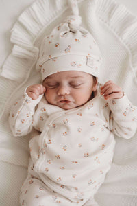 Een vredige pasgeboren baby die slaapt, gekleed in een schattig bedrukt Yumi Baby Broekje Peach Blossom onesie en bijpassend hoedje, liggend op een zacht wit oppervlak met de armen zachtjes omhoog bij het gezicht.