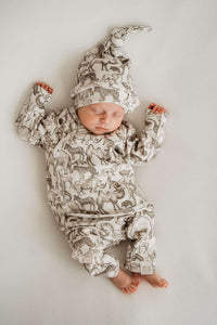 Een gezellige baby gekleed in een knus Yumi Baby Broekje Little Safari-outfit met een schattig bijpassend hoedje, ligt in een geweven mand, omringd door zachte, verkreukelde dekens, tevreden en vredig.