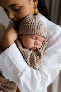 Een vredige baby slaapt heerlijk, gehuld in een Yumi Baby gebreide trui cacao schatje, liggend op een zacht beige dekentje.