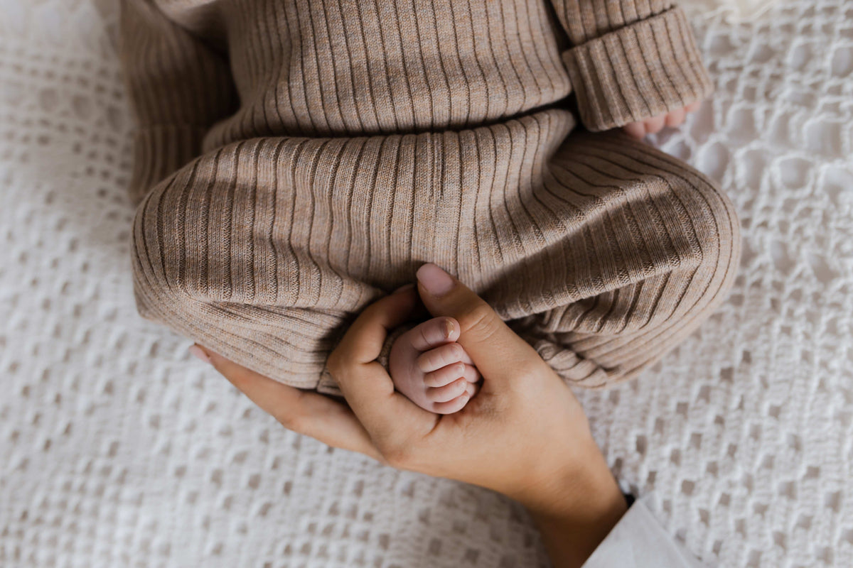 Een vredige baby slaapt heerlijk, gehuld in een Yumi Baby gebreide trui cacao schatje, liggend op een zacht beige dekentje.