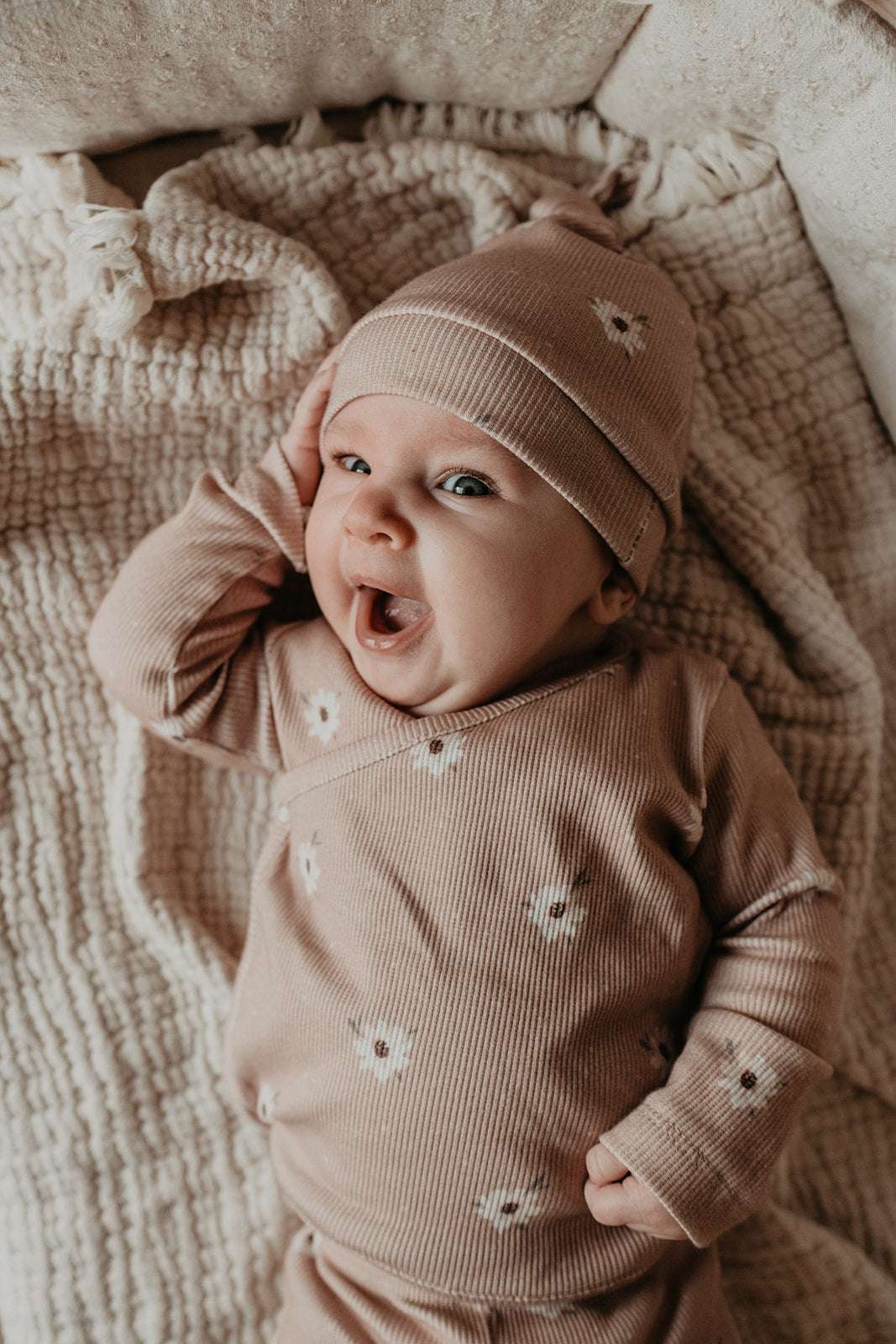 Een pasgeboren baby kleding in een gezellige beige outfit met sterpatronen, liggend op een zachte deken en draagt een kledingstuk Yumi Baby Muts Zoë met Dots.